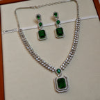Jewelry set with necklace and earrings featuring green gemstones on a beige background.
