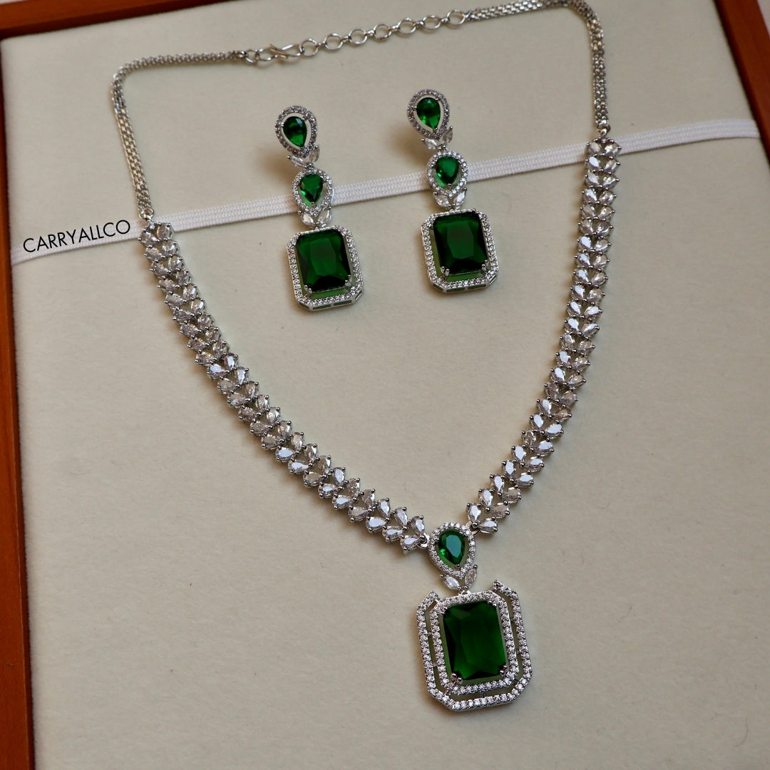 Jewelry set with necklace and earrings featuring green gemstones on a beige background.