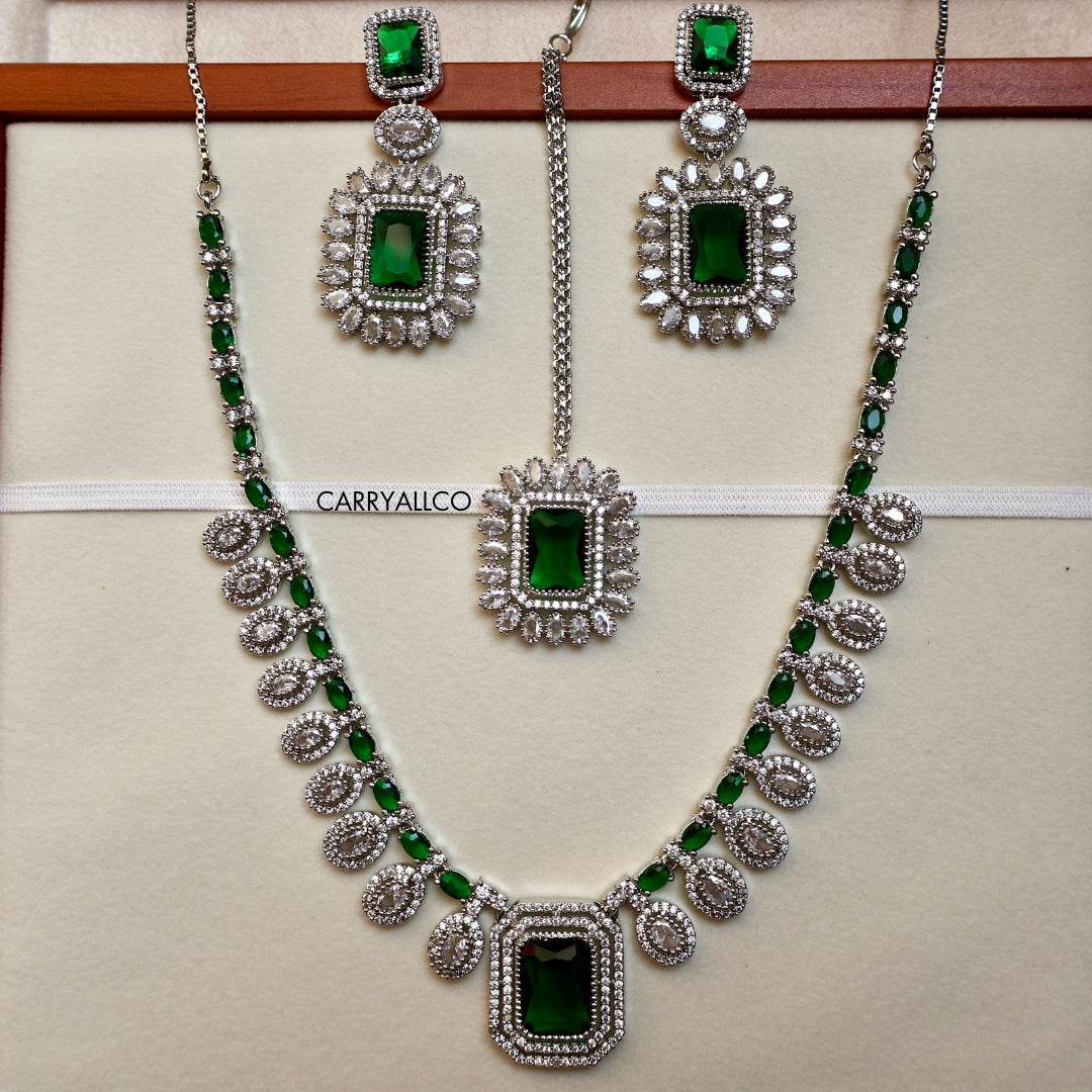 Jewelry set with necklace and earrings featuring green stones and silver accents on a beige background.