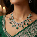 Woman wearing a green and silver necklace with emerald stones and matching earrings.