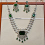 Jewelry set with necklace and earrings featuring green gemstones on a beige background.