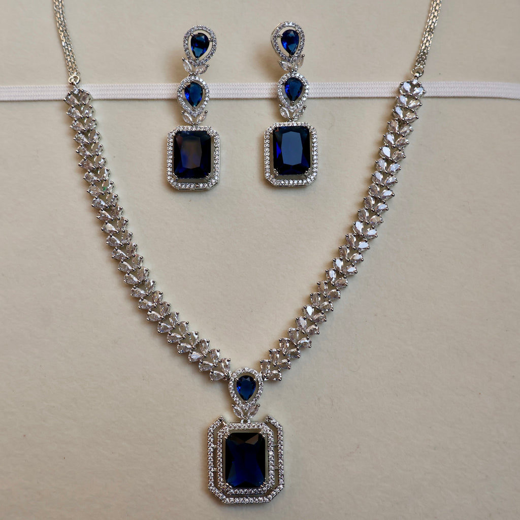 Jewelry set with necklace and earrings featuring blue gemstones on a beige background