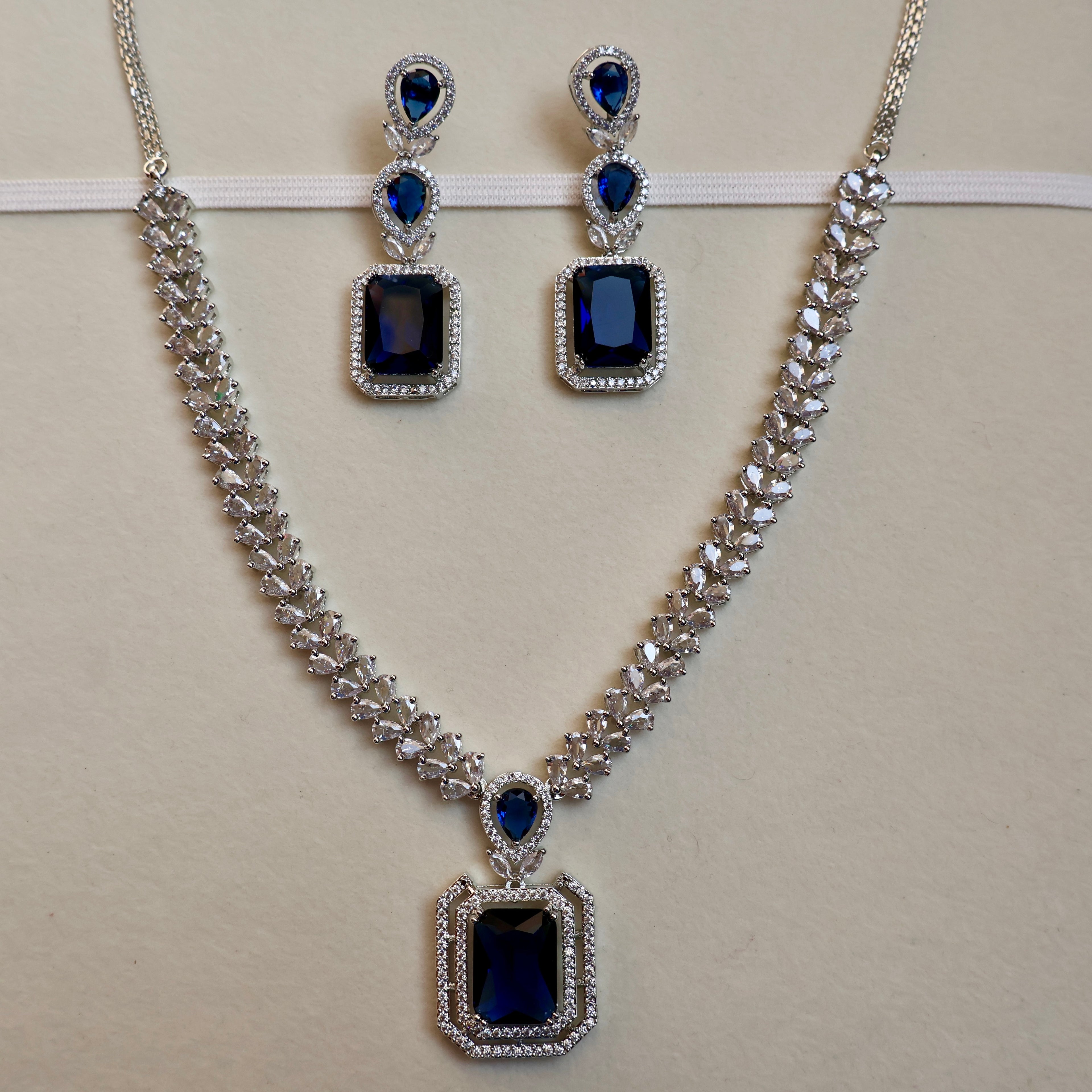 Jewelry set with necklace and earrings featuring blue gemstones on a beige background