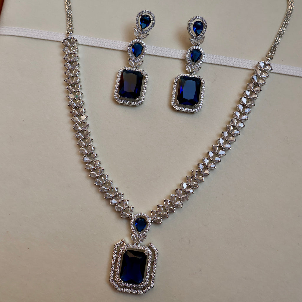 Jewelry set with necklace and earrings featuring blue gemstones on a beige background