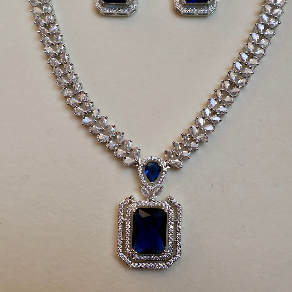 Jewelry set with necklace and earrings featuring blue gemstones on a light background