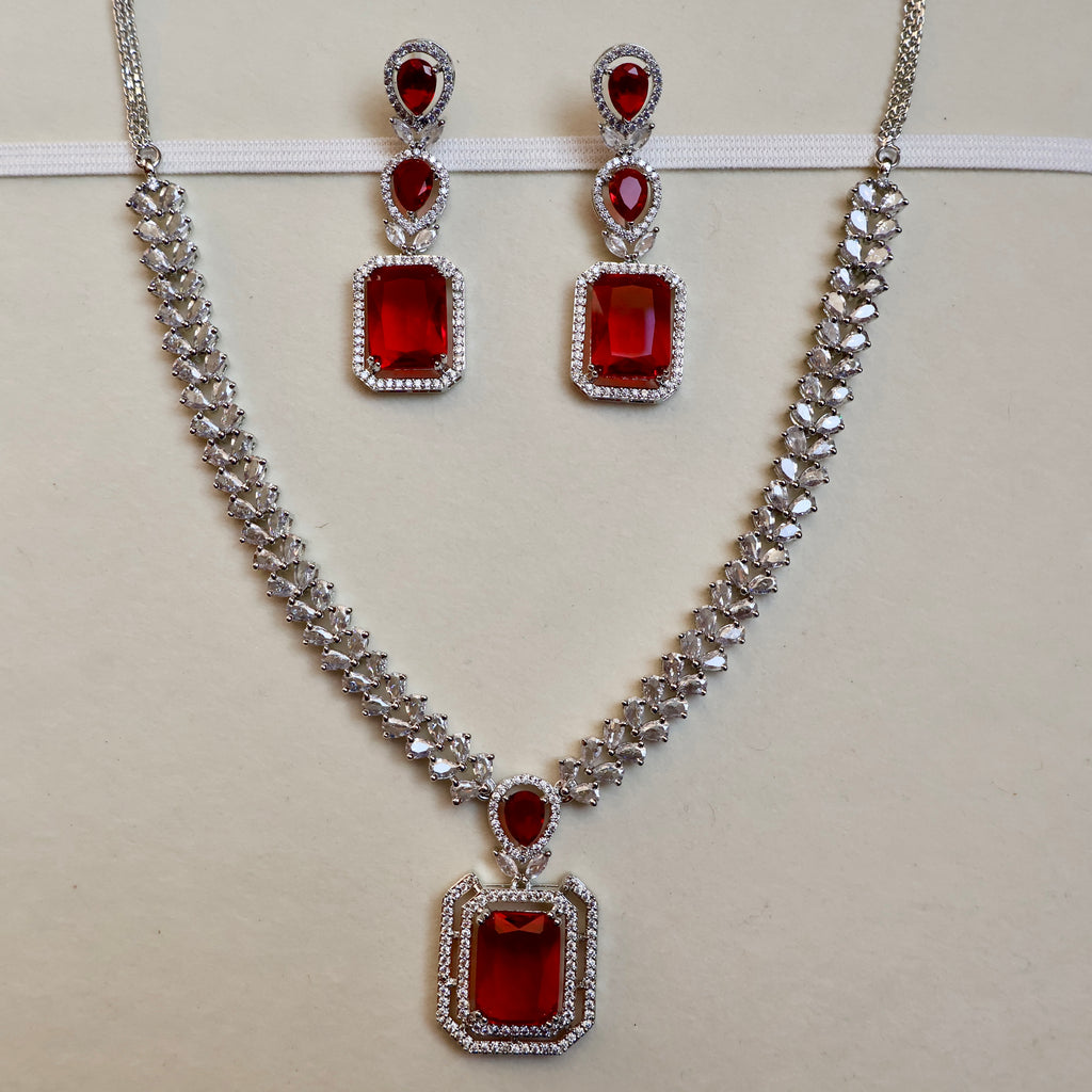 Jewelry set with necklace and earrings featuring red gemstones on a light background