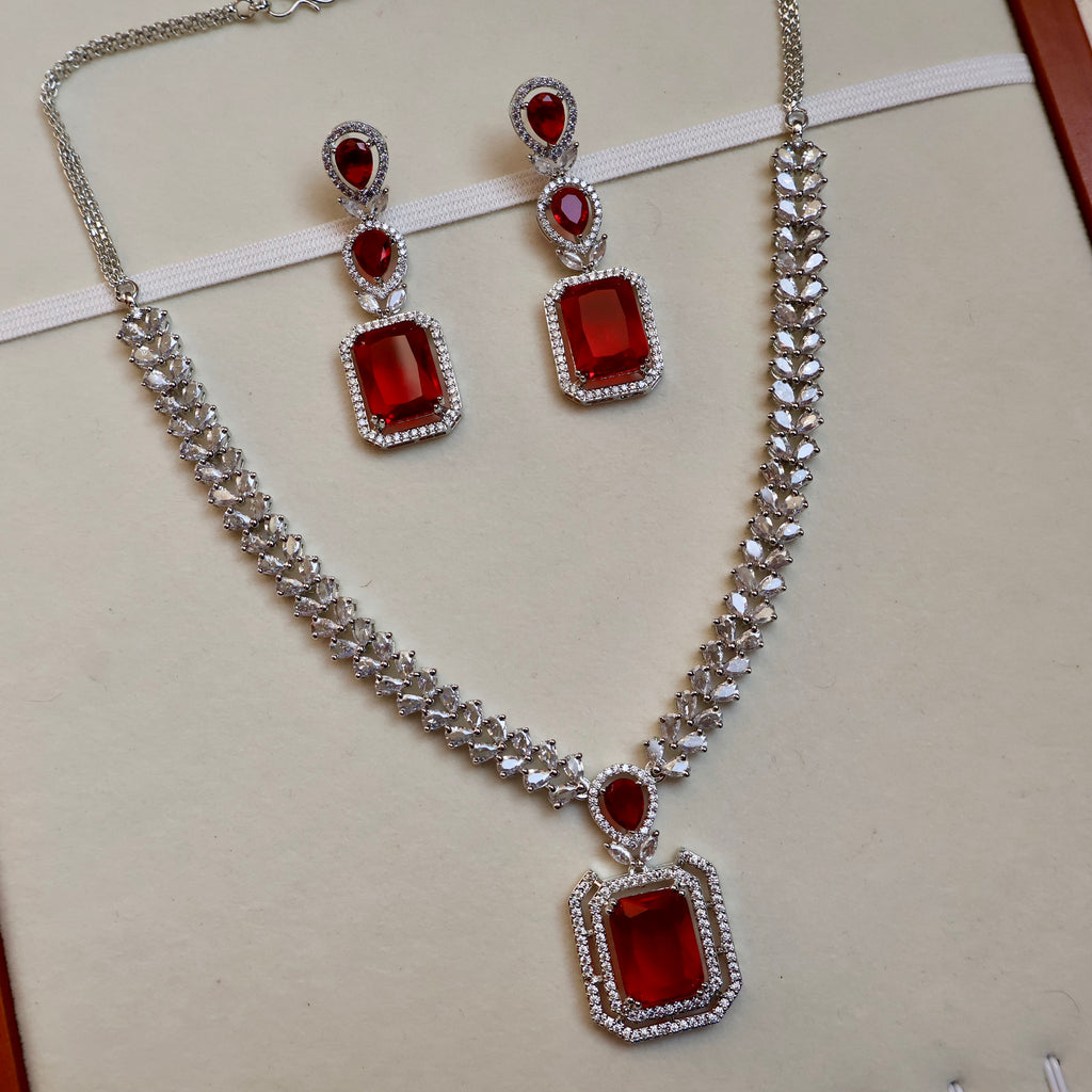 Jewelry set with necklace and earrings featuring red gemstones on a light background