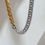 Two braided chain necklaces, one gold and one silver, on a light gray background.