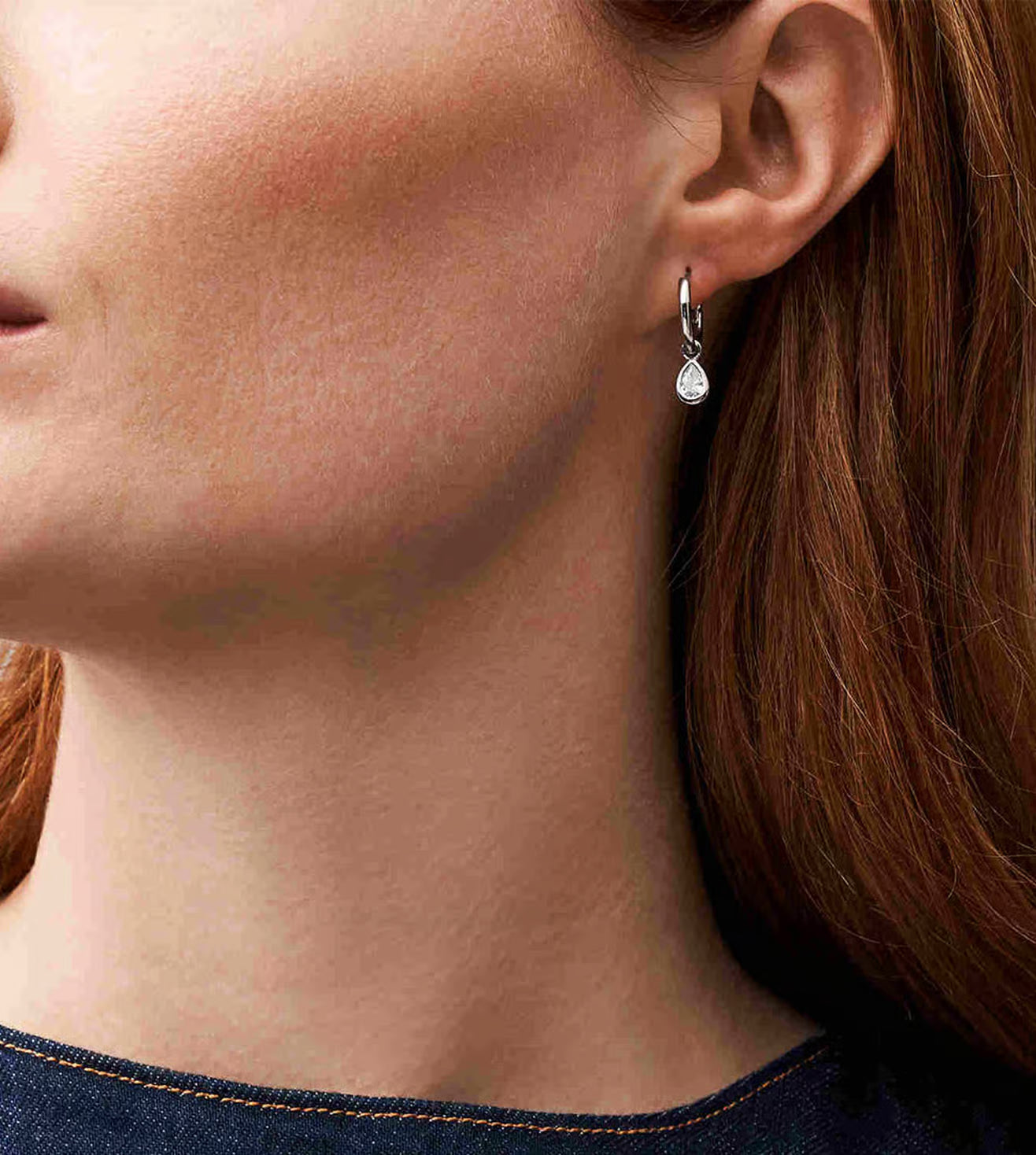Close-up of a woman wearing a silver earring with a teardrop-shaped gemstone.