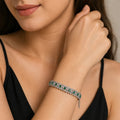 Close-up of a woman wearing a bracelet with emerald stones on a neutral background