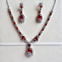 A red and silver jewelry set featuring a necklace, matching earrings, and a headpiece displayed on a textured white background.