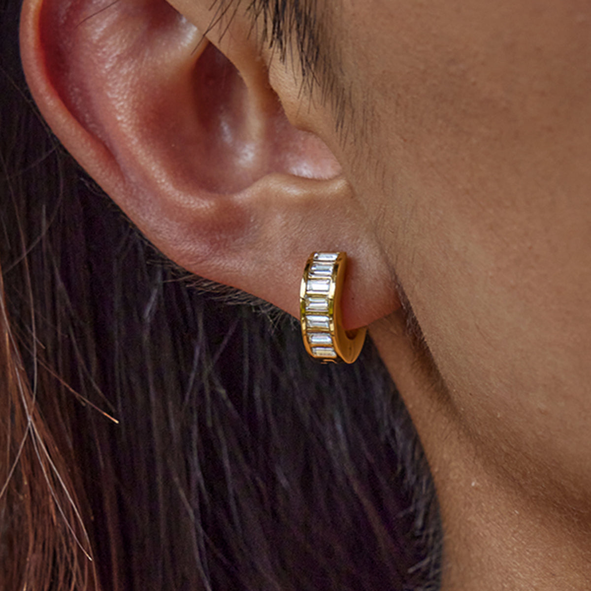 Gold hoop earring with embedded stones worn by a person