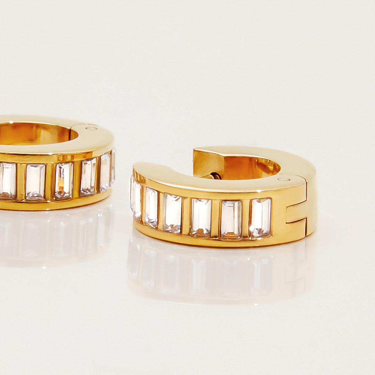 Gold hoop earrings with embedded stones on a light background