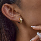 Close-up of an ear wearing a gold hoop earring with a blurred background