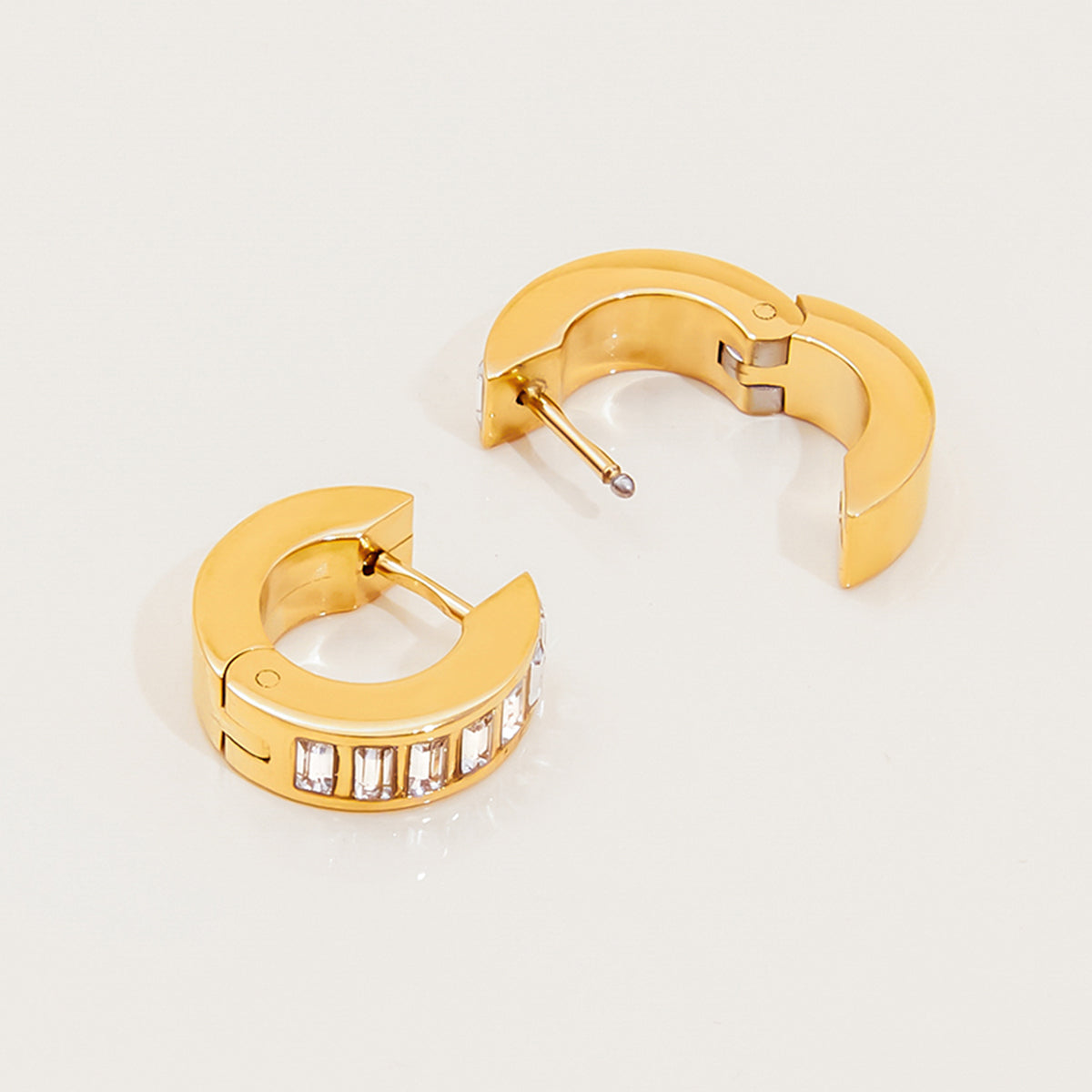 Gold hoop earrings with embedded stones on a light gray background