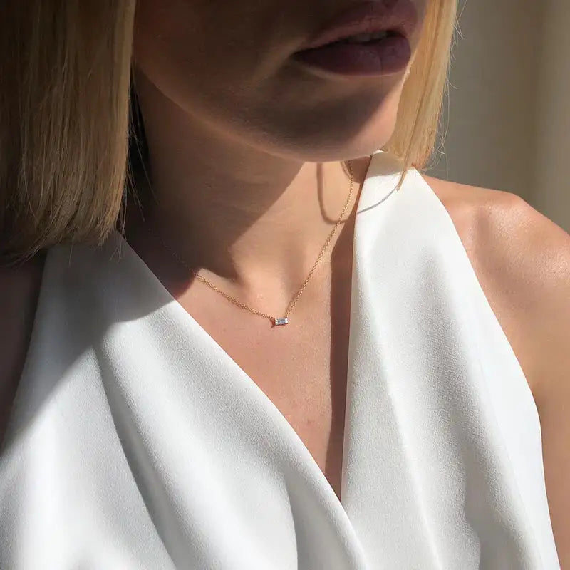 Close-up of a person wearing a white top and a delicate necklace with a small pendant.