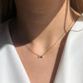Gold necklace with a small rectangular pendant worn by a person in a white top.