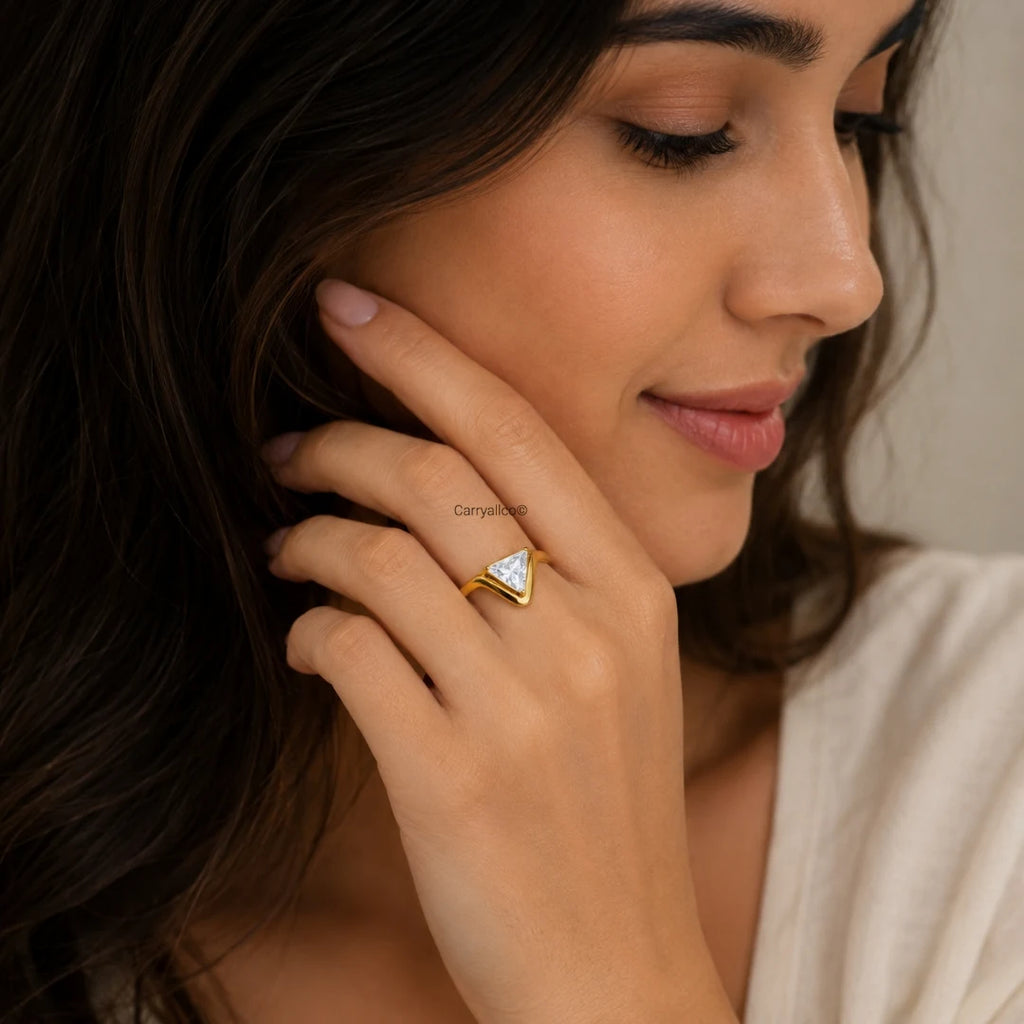 Woman wearing a gold ring with a triangular gemstone, touching her ear.
