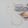 Gold necklace on a light gray surface with sunglasses and a magazine in the background