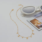 Gold necklace on a light gray surface with sunglasses and a magazine in the background