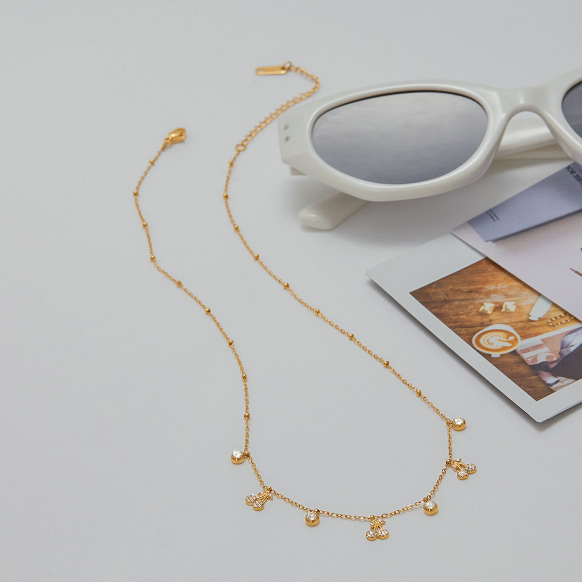 Gold necklace on a light gray surface with sunglasses and a magazine in the background