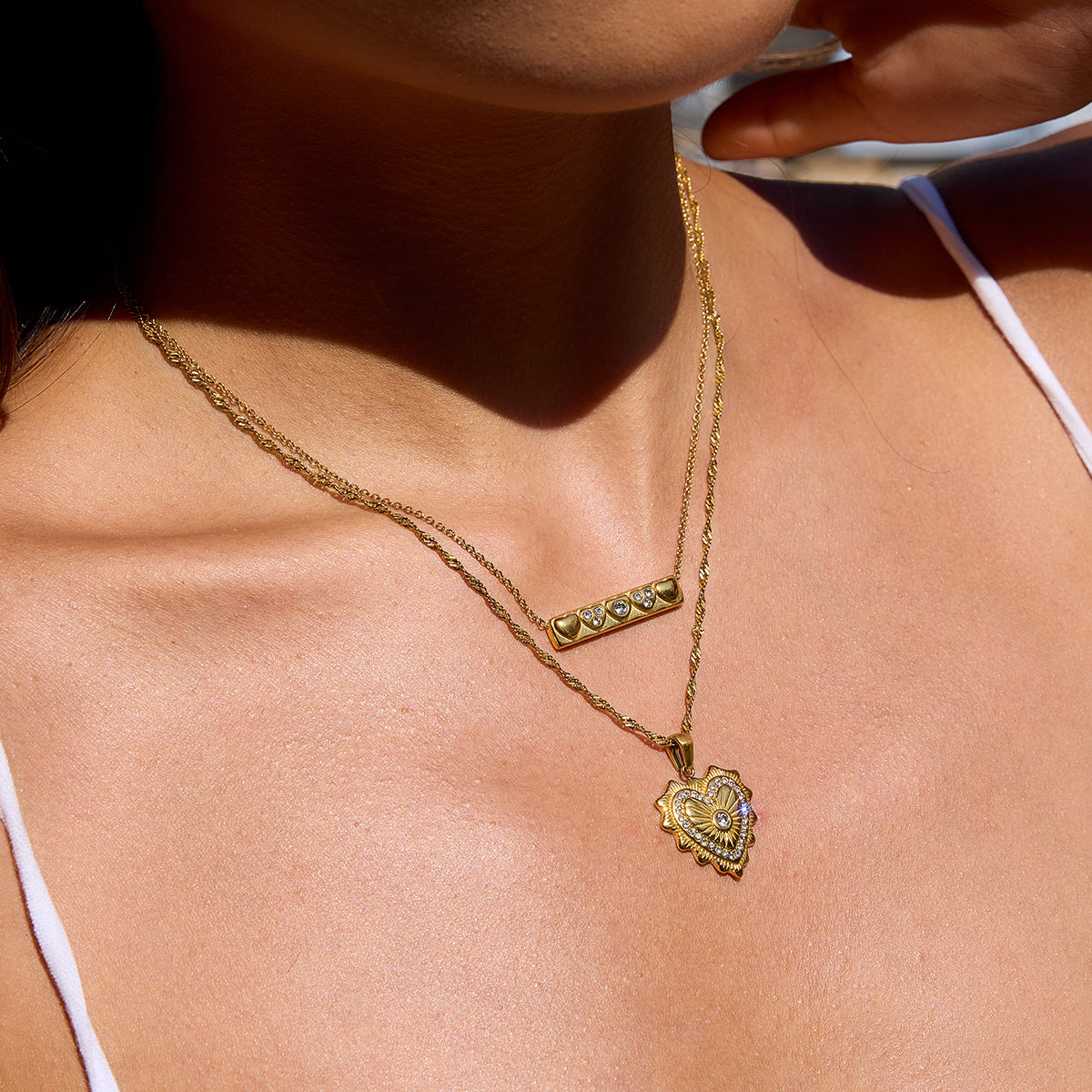 Close-up of a person wearing two gold necklaces with heart pendants.