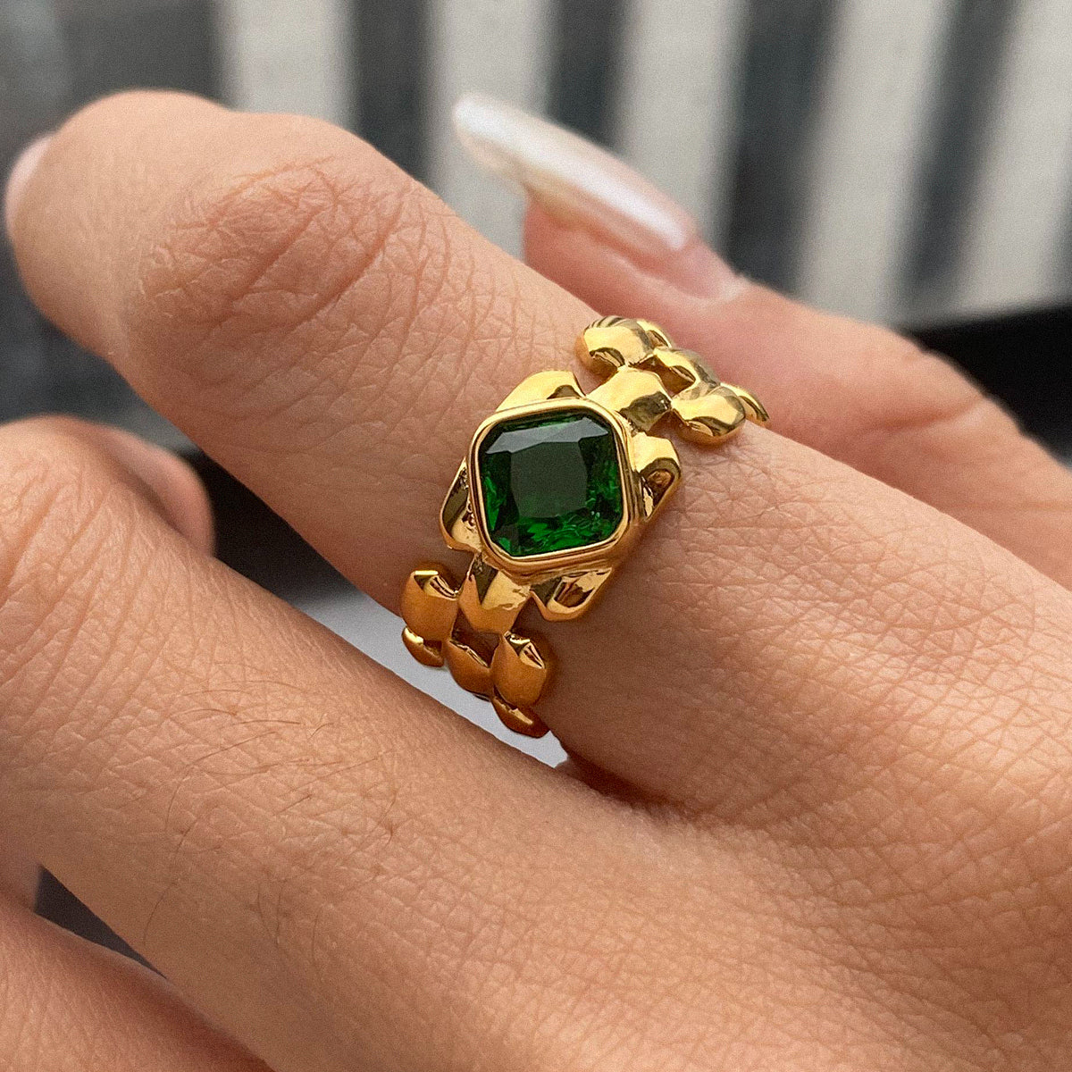 Gold ring with a green gemstone on a finger against a blurred background