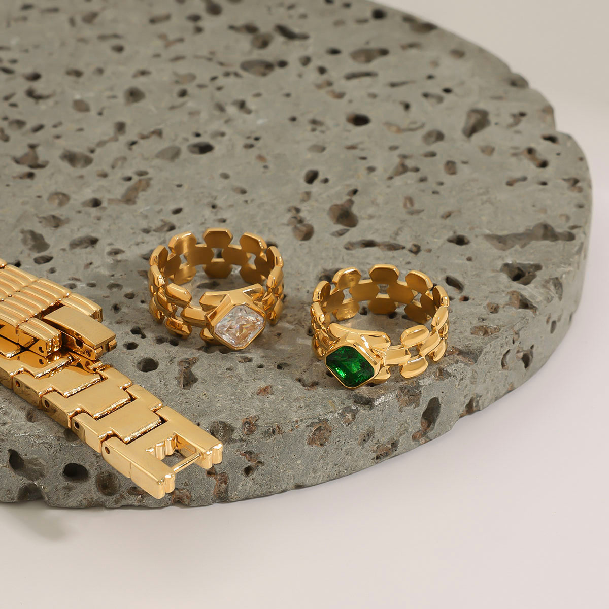 Gold jewelry set with rings and a bracelet on a textured stone surface