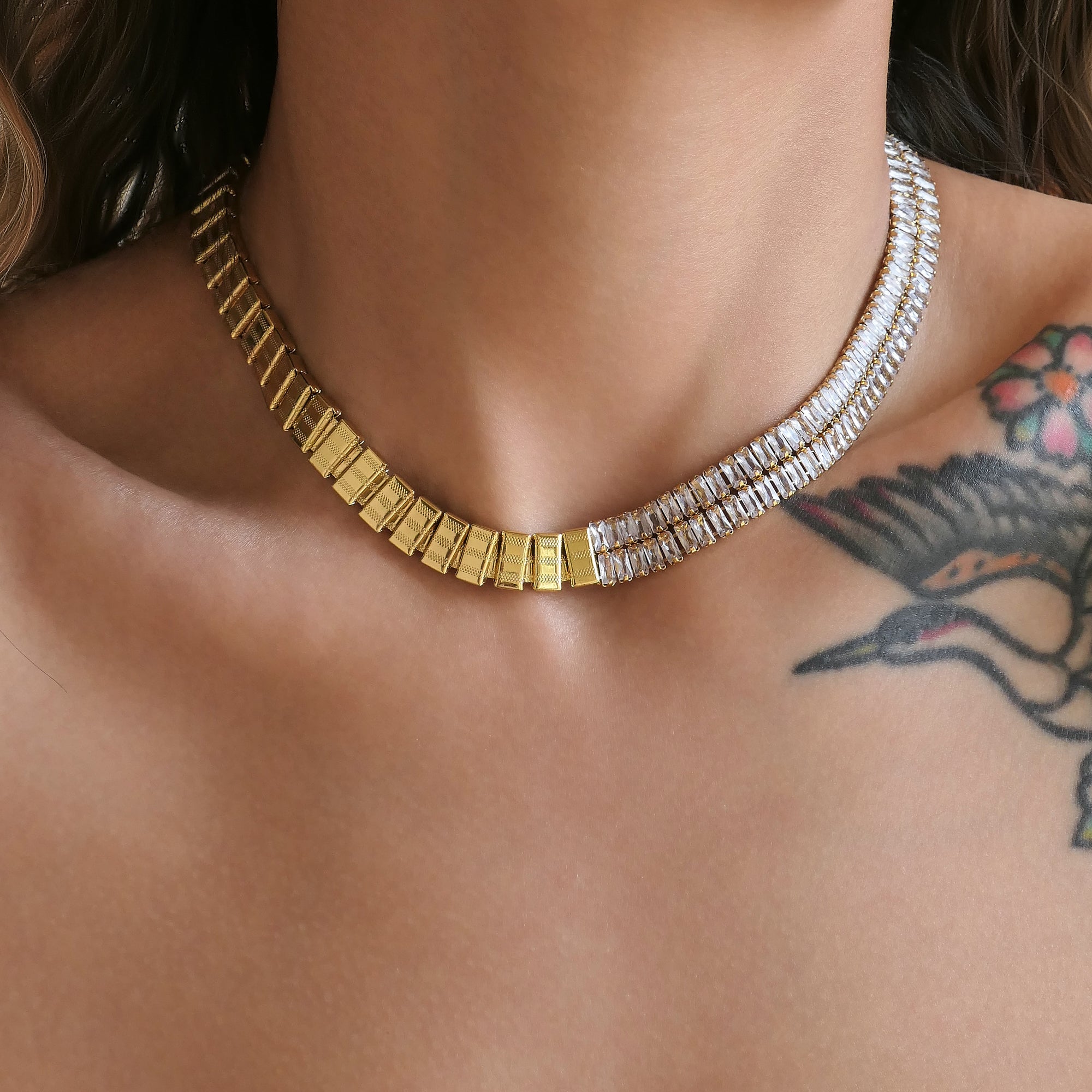 Gold and silver necklace on a person with visible tattoos