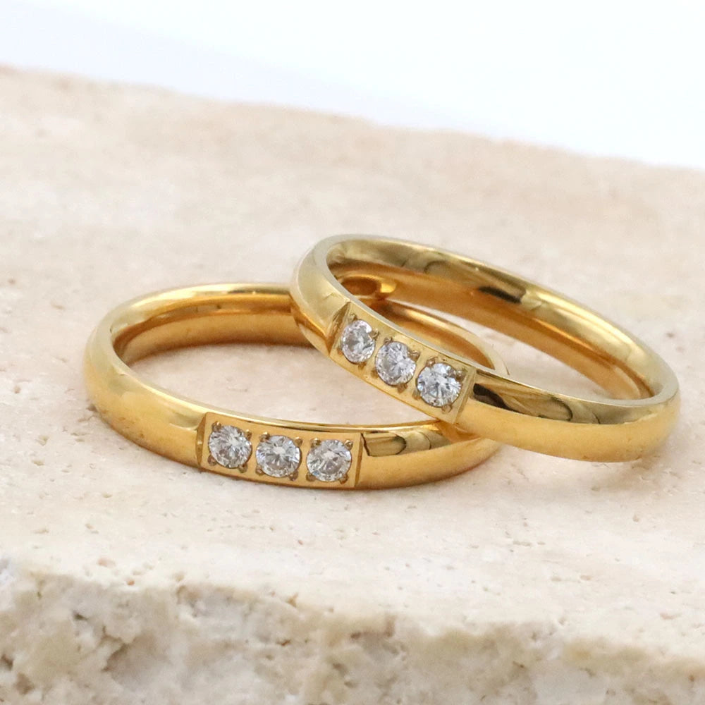 Two gold rings with embedded diamonds on a beige stone surface