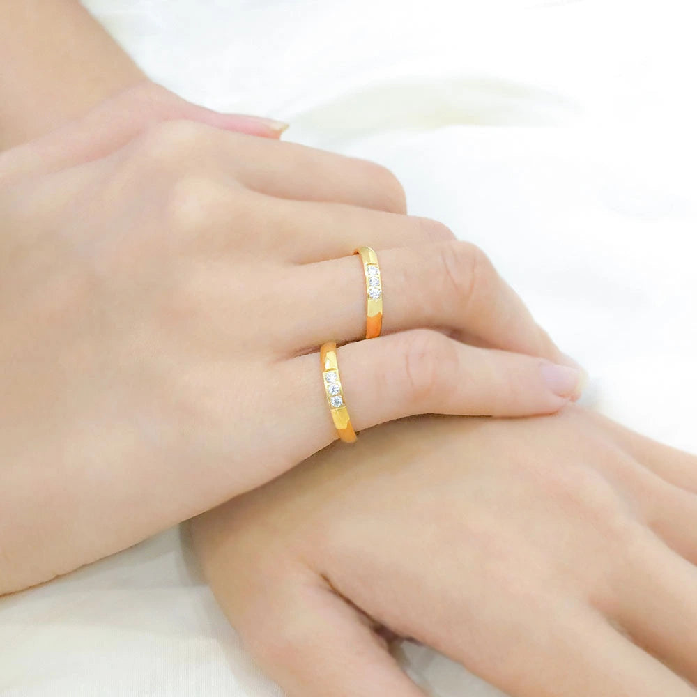 Two hands wearing gold rings with small stones on a light background