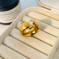 Gold ring with a diamond on a beige jewelry box with a bottle in the background
