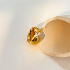 Gold earring with a clear gemstone on a beige stand against a light background