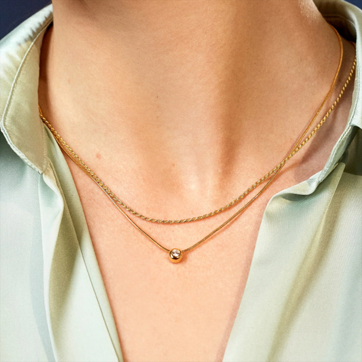 Gold necklace with a small round pendant on a person wearing a light green shirt.