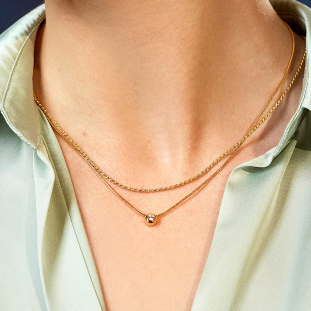 Gold necklace with a small round pendant on a person wearing a light green shirt.