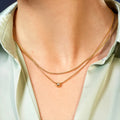 Gold necklace with a small round pendant on a person wearing a light green shirt.