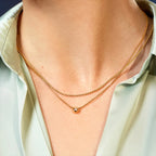 Gold necklace with a small round pendant on a person wearing a light green shirt.