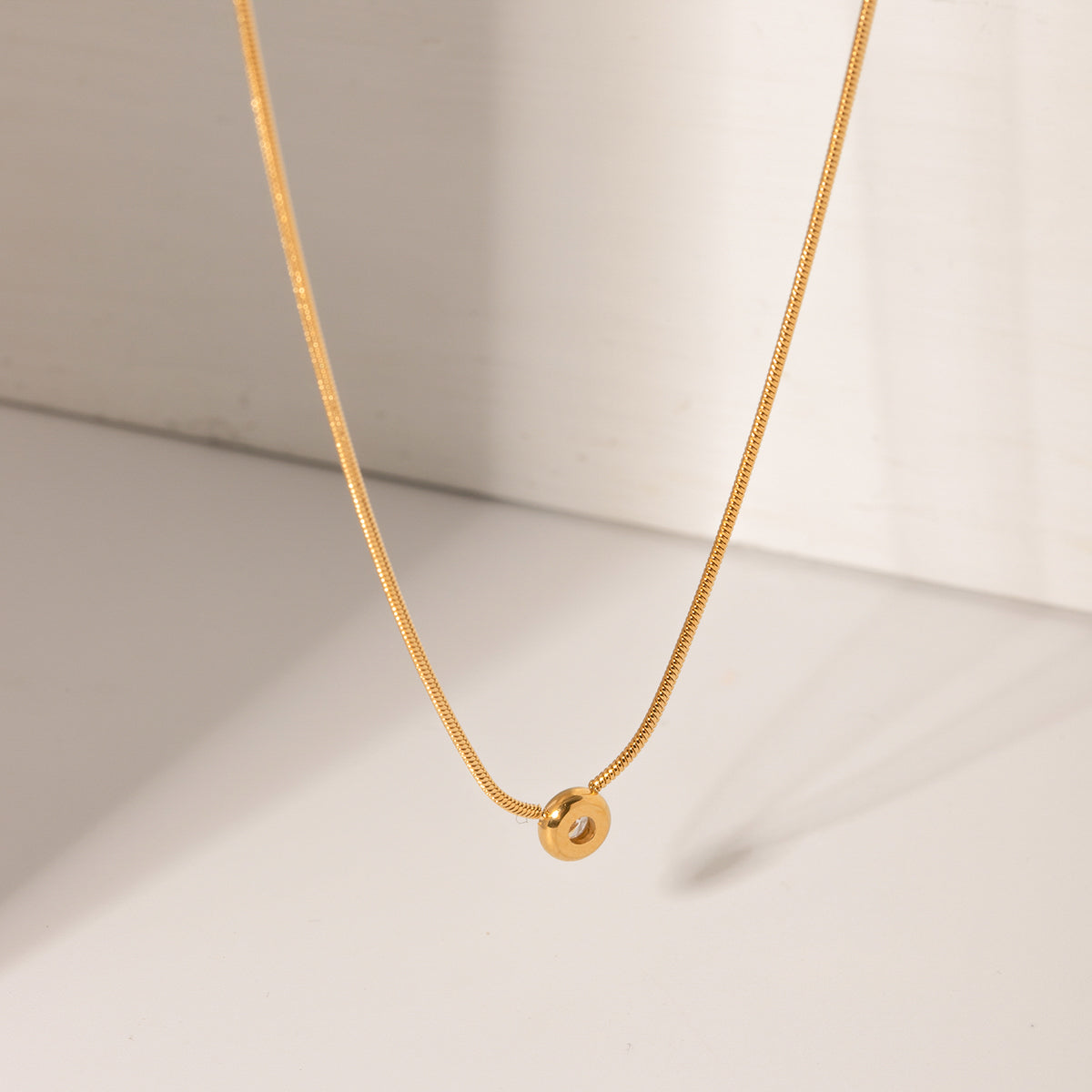 Gold necklace with a round pendant on a light beige background