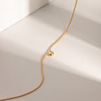 Gold necklace with a small gemstone on a light beige background