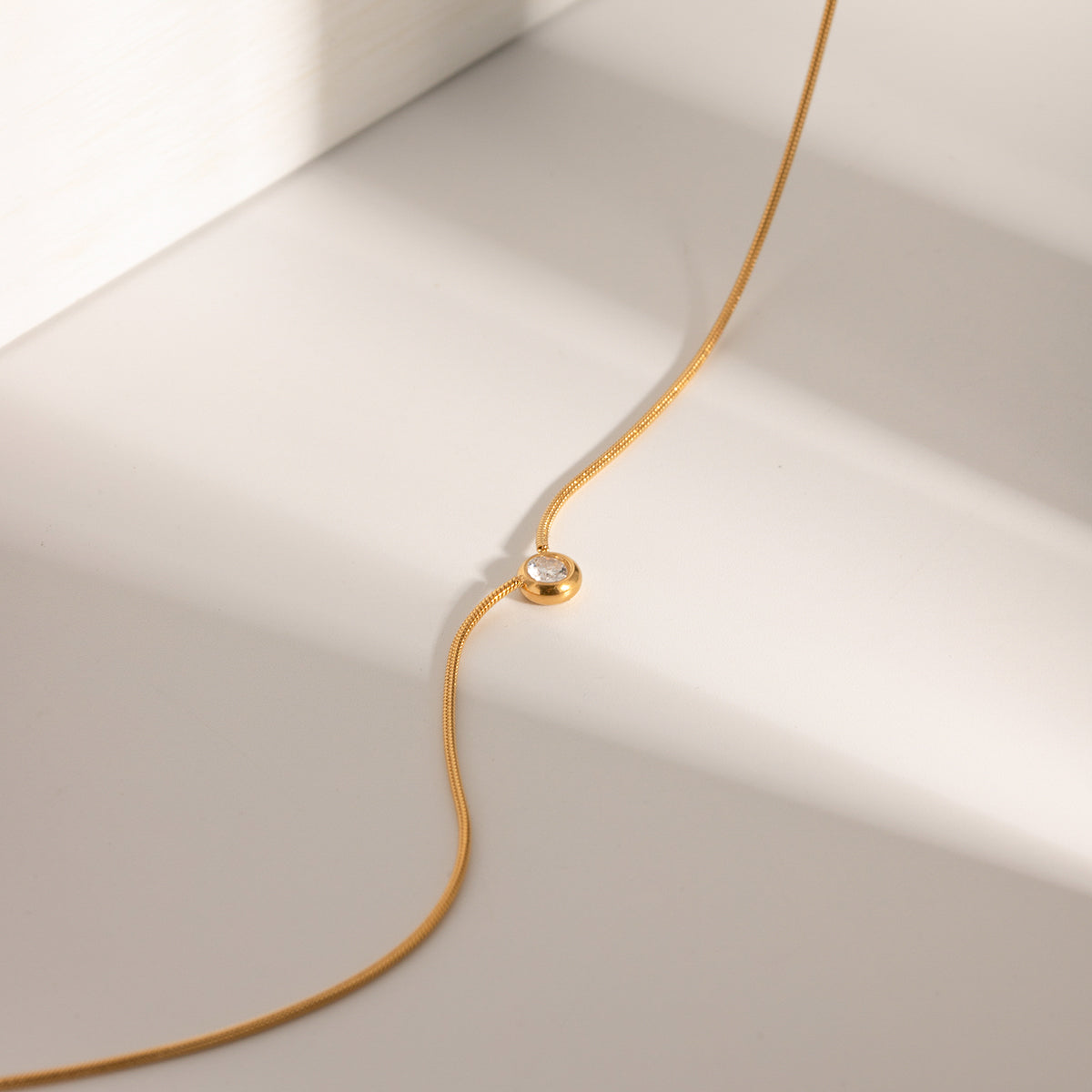 Gold necklace with a small gemstone on a light beige background