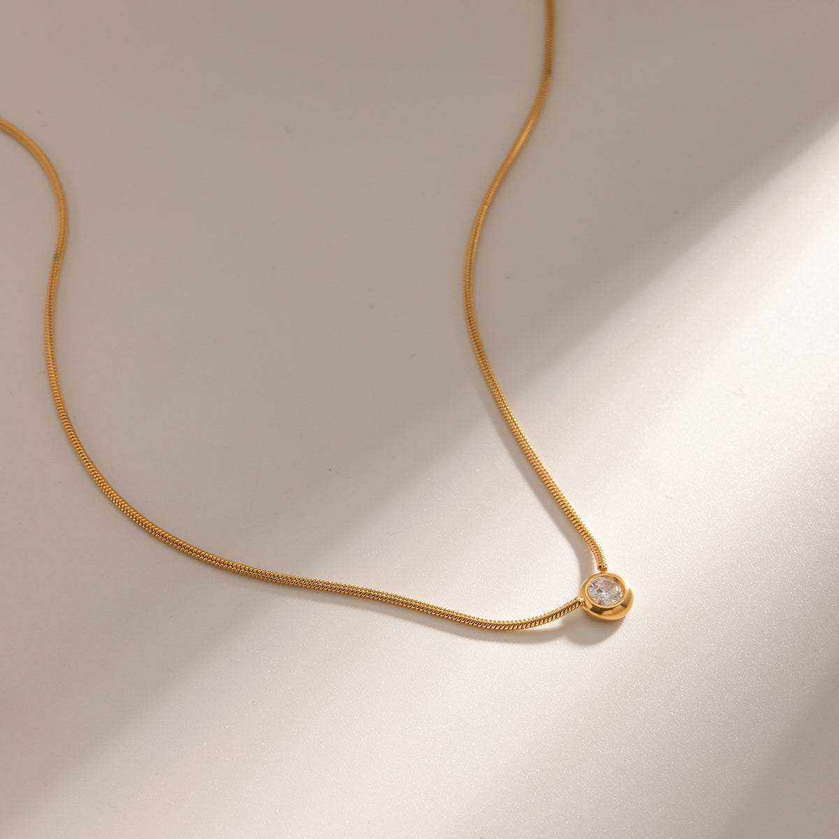 Gold necklace with a small round pendant on a beige background