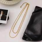 Gold chain necklace on a white surface with a black leather bag and photo album.