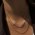Close-up of a person wearing two gold chains on their neck against a dark background