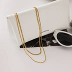 Gold chain necklace draped over a white clutch with sunglasses on a light gray background