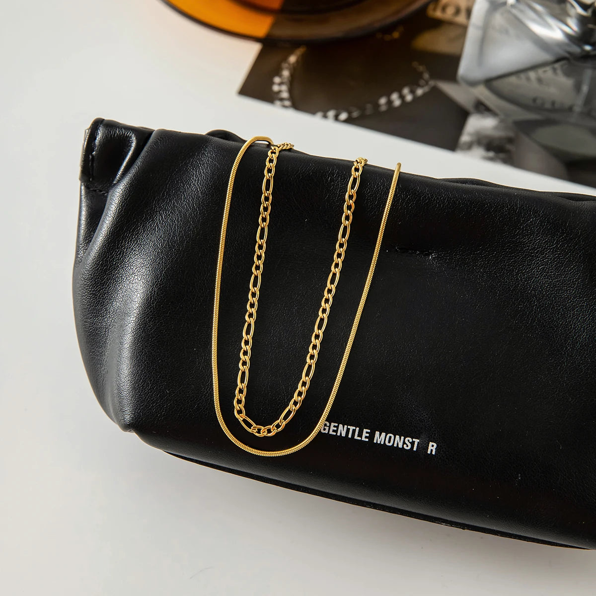 Gold chain on a black clutch with 'GENTLE MONSTER' branding.