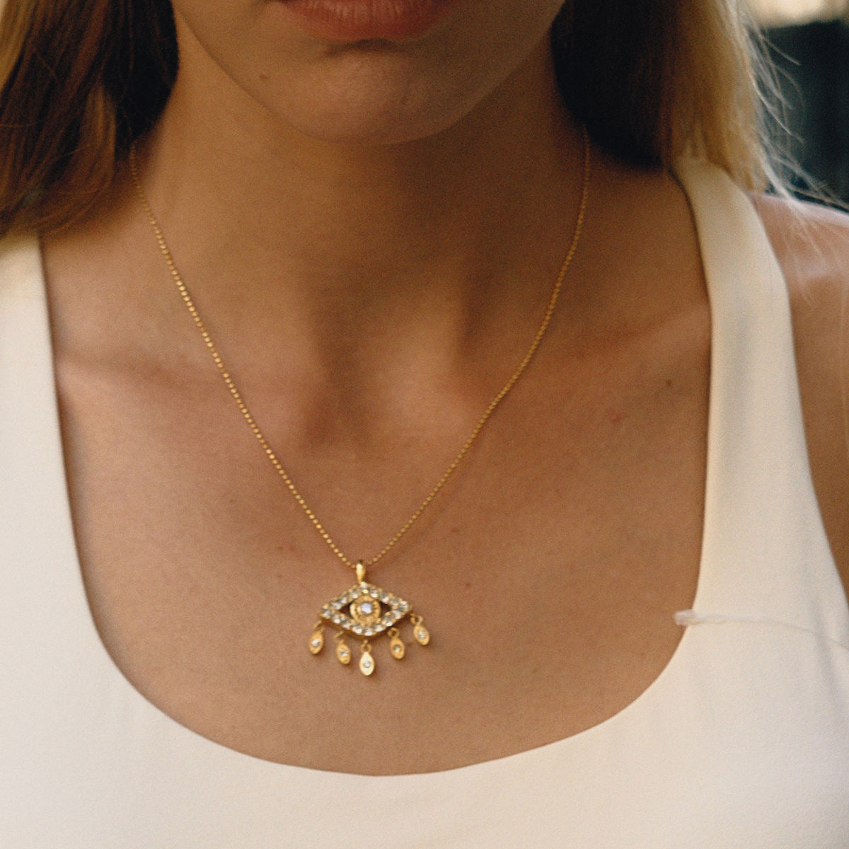 Gold necklace with a pendant worn by a person in a white top.