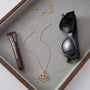 Gold necklace, tube of lipstick, and black sunglasses on a gray surface