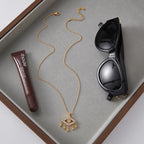 Gold necklace, tube of lipstick, and black sunglasses on a gray surface