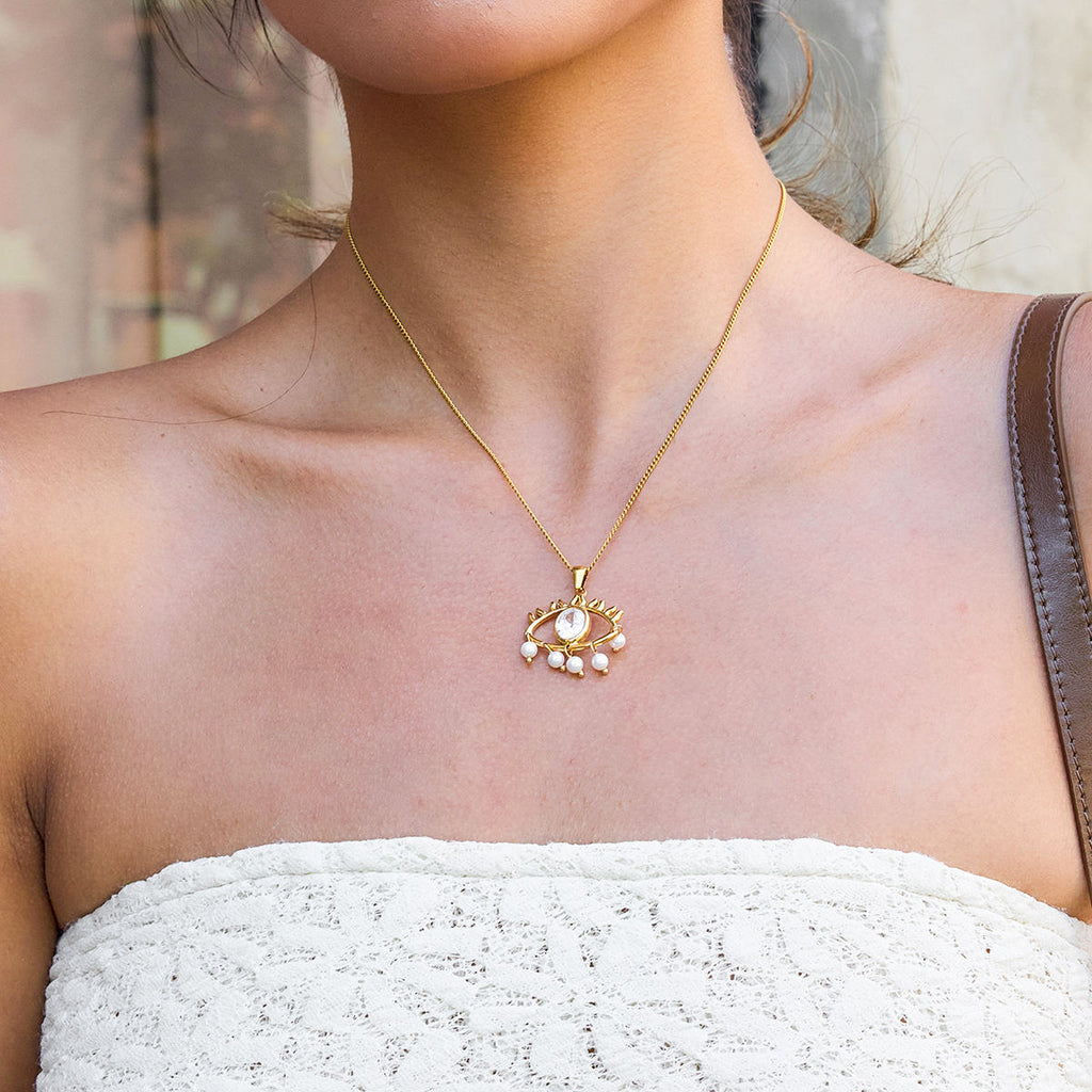 Gold necklace with a pendant worn by a person in a white top.