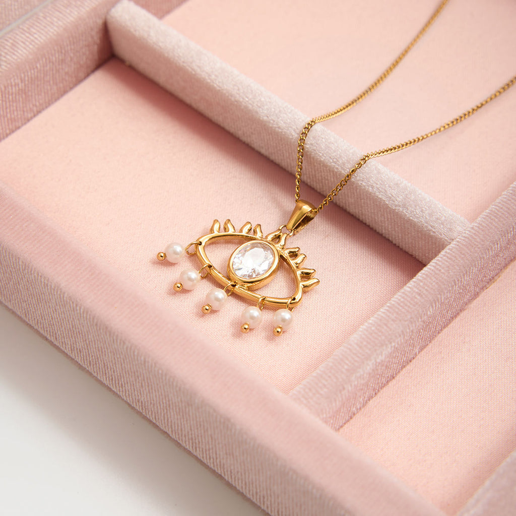 Gold necklace with a heart-shaped pendant and pearl accents on a pink velvet surface